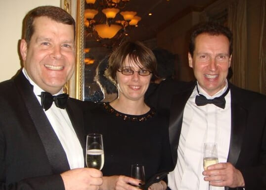 Three people at a corporate evening event with Champagne glasses in hand