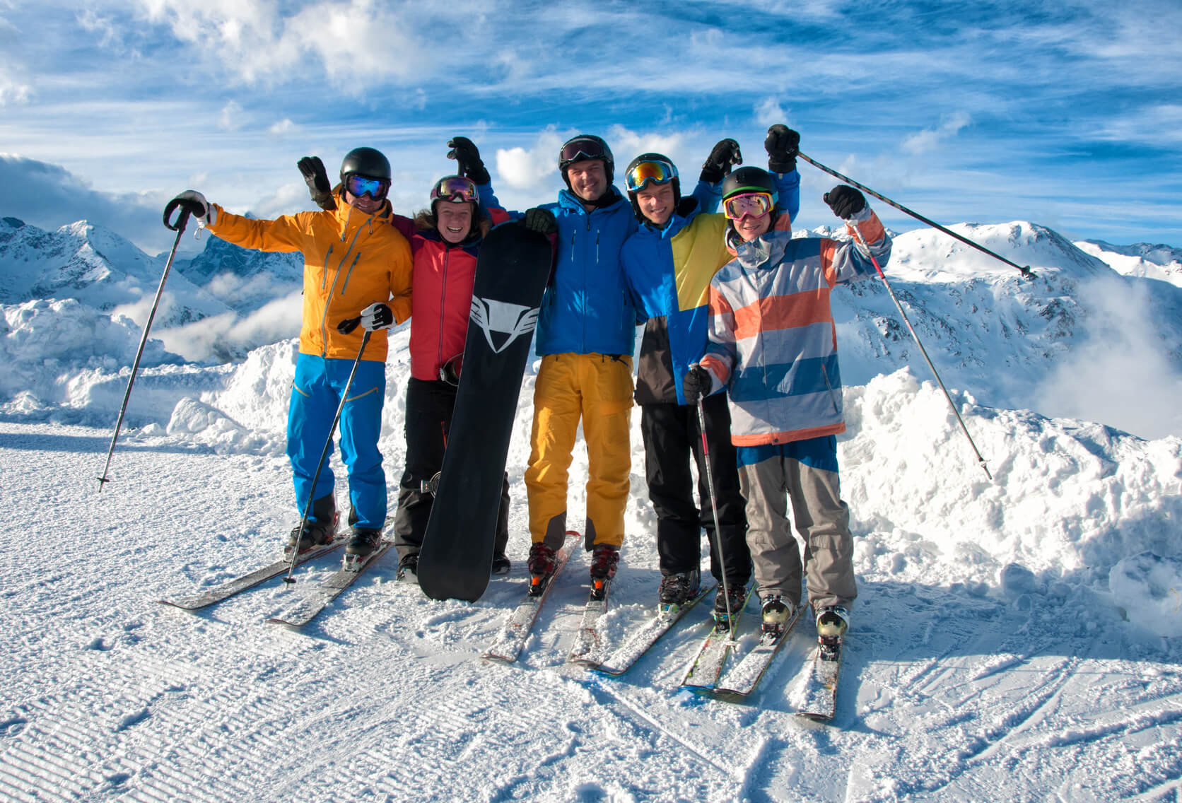 Group of 5 young men with skis on top of a mountain in the snow