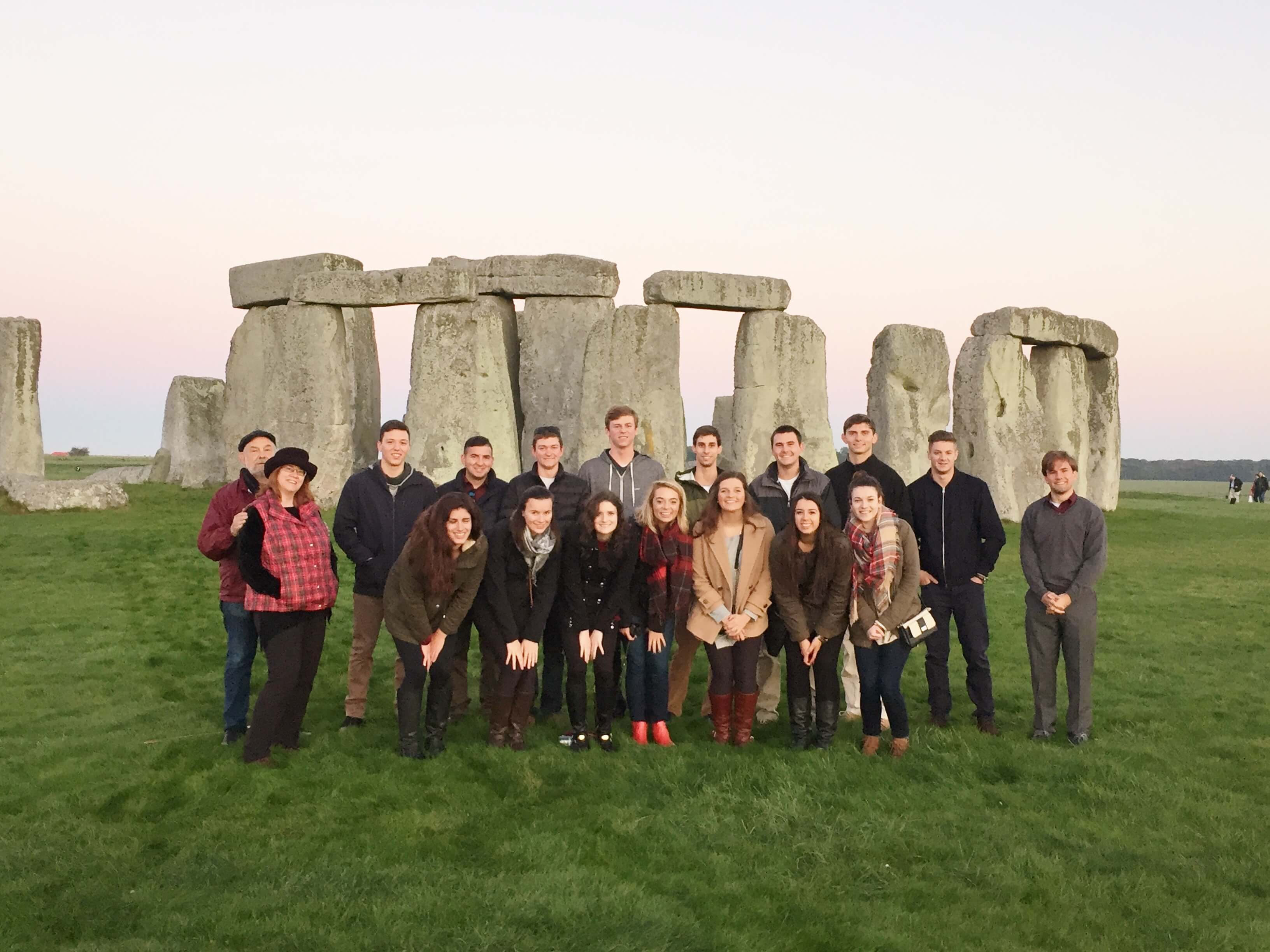 Group of University students on educational tour with Stonehenge at dawn behind them