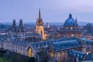 View from a height over the rooftops of Oxford city, the historic buildings and the landmarks of the university city. Night. Buildings lit up.