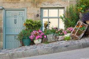 The Beach House, Robin Hood's Bay, North York Moors National Park. A house on a street on a steep hill. Flowering plants in pots outside the door and windows.